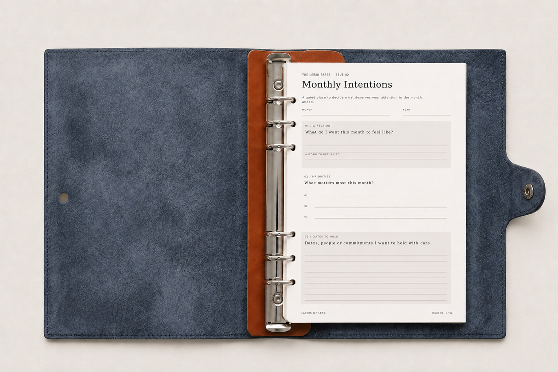 The LeRoi Paper Issue 02 Monthly Intentions printable displayed in a navy leather six-ring journal