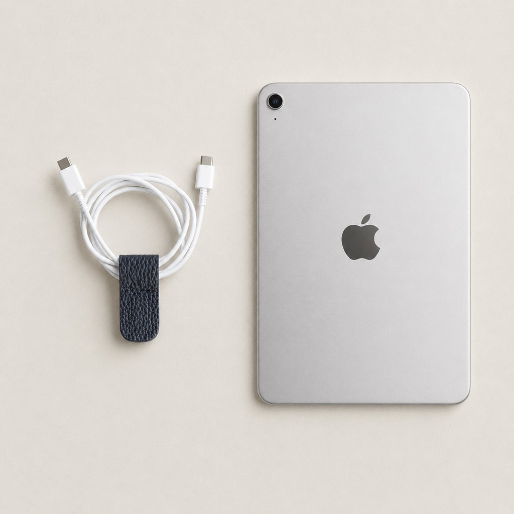 Cord Wrap in Dark Navy German Togo leather beside a charging cable and tablet.